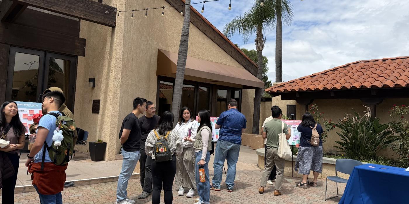 Community members gathered in an outdoor courtyard during a public event, with display boards and a registration table nearby.
