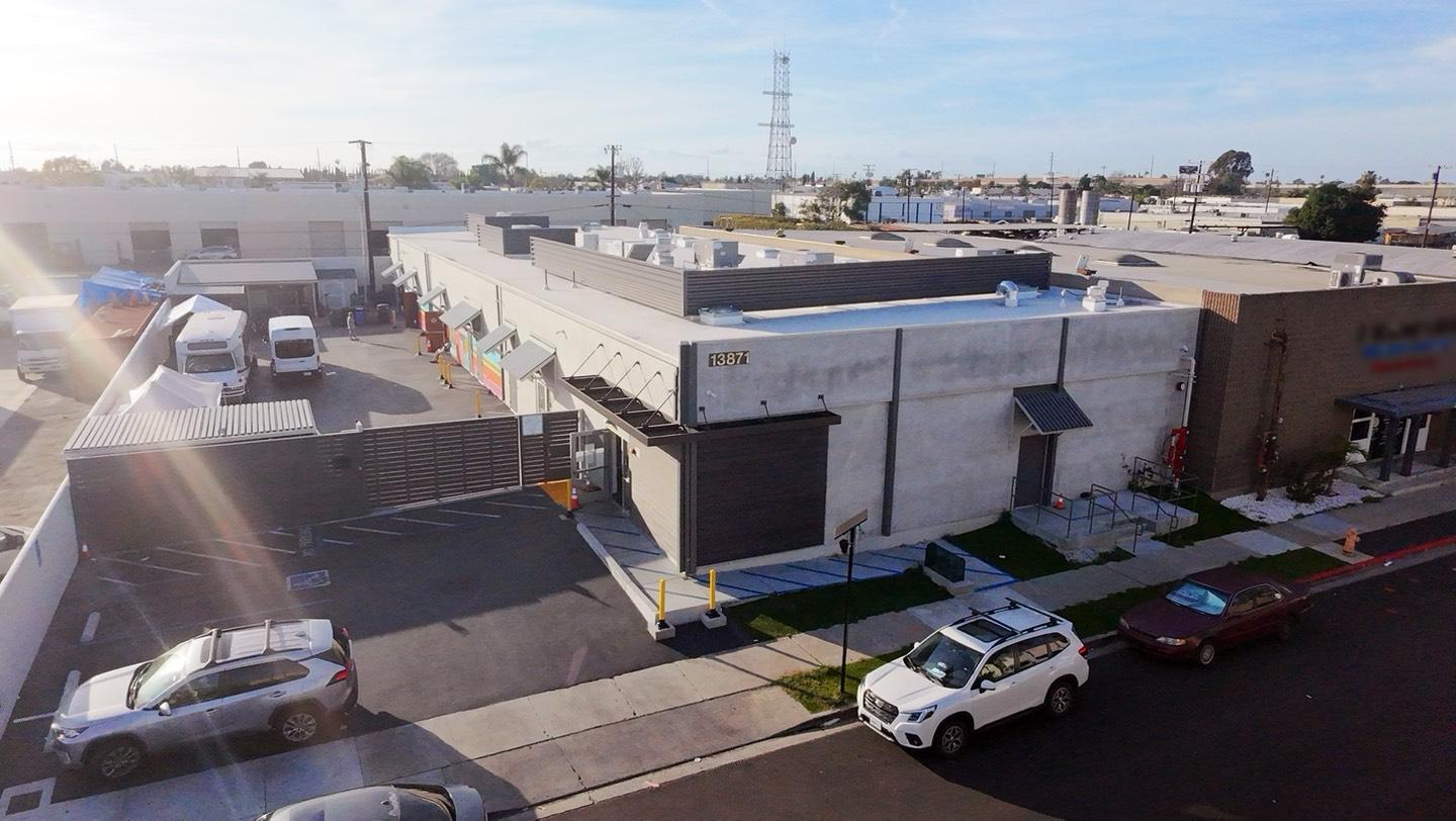 Aerial photograph of a commercial warehouse building at 13871, with parked SUVs and vans on a sunny day.